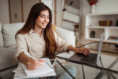Binlerce yıllık Avrupalı bayanın bilgisayarda yazı yazması ve oturma odasının iç kısımlarına not alması ile meşgul. Çoklu görev, serbest çalışma ve evde iş, cihaz ve eğitimle öğrenim