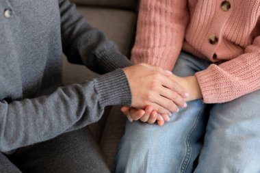 Avrupalı milenyum annesi, iç mekanda el ele tutuşarak üzgün genç kızı sakinleştiriyor. Evde aşk, destek, ilgi, tavsiye ve ilişkiler