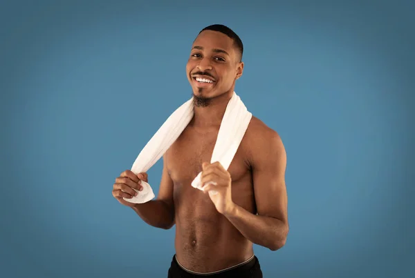 赤裸的年轻非洲裔美国人 肩膀上披着毛巾 背景是蓝色的 对着相机笑 有运动的黑人男子在健身房锻炼 复制空间 — 图库照片