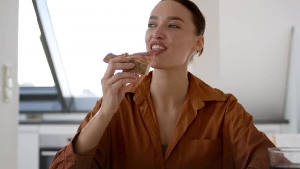 食事の楽しさをカンニング 若い幸せな女性は 新鮮なピザを取り それをかむ キッチンでの食品配達サービスを楽しんで ショットを追跡し スローモーション フリースペース — ストック動画