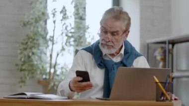 İş ve aktif emeklilik. Ofiste dizüstü bilgisayarda çalışan kıdemli bir iş adamı, telefona cevap veriyor ve ortakla projeyi tartışıyor, izleme çekimi, yavaş çekim, serbest alan