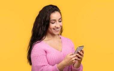 Bin yıllık beyaz kadın akıllı telefonuyla günlük daktilo kullanıyor, sosyal ağlarda sohbet ediyor sarı arka planda izole edilmiş, yakın plan, stüdyo. İnternet sörfü, blog, yaşam tarzı iyi haberler