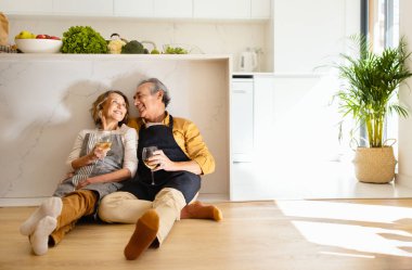 Mutlu kıdemli eşler mutfakta şarap içerler, yerde otururlar, kucaklaşırlar ve sohbet ederler, sohbet ederler, birlikte vakit geçirirler, kopyalama alanı, tam boy