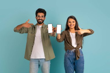 Gündelik kıyafetlerle gezen, beyaz ekranlı telefonları olan mutlu, çok kültürlü genç bir çift mobil uygulama reklamı için model, renkli stüdyo arka planı.