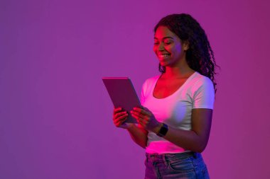 Siyah kadın Neon Light 'ta duruyor ve dijital tablette interneti tarıyor, Mutlu Afro-Amerikan kadın online alışveriş veya oyun için modern Gadget kullanıyor, Mor Arkaplan üzerine poz veriyor