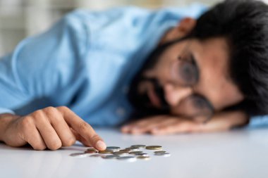 Yoksulluk ve para yokluğu. Üzgün Hintli adam evde masaya yaslanırken madeni para sayıyor, depresyondaki genç doğulu adam mali kriz ve iflastan muzdarip, seçici odaklanma, kapatma