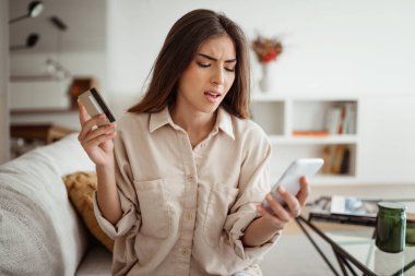 Minimalist oturma odasındaki telefona bakan binlerce yıllık Avrupalı bir kadının kredi kartıyla morali bozuk. Çevrimiçi alışveriş, finans bankacılığı, sırayla hata, satış sorunları