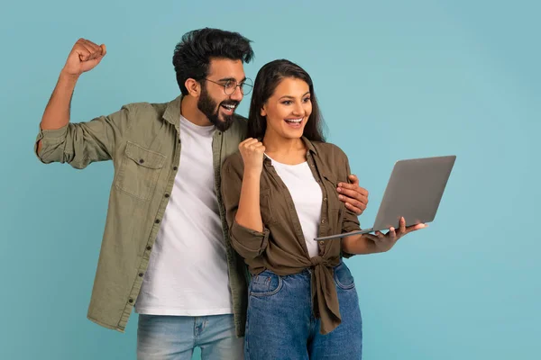 青のスタジオの背景にラップトップを使用して 感情的な幸せな陽気な若いインドのカップルのギャンブルオンラインでは 成功を祝うために 拳を上げて排除します オンラインベット キャッシュバック プレゼント — ストック写真