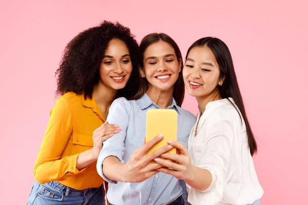 ピンク色のスタジオを背景に立ち 携帯電話で自撮りをする多様な女性たち 女性の友情 友人が一瞬で写真を撮る — ストック写真