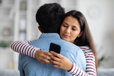 Oldukça uzun saçlı genç bir doğu kadını erkek arkadaşına sarılırken akıllı telefondan erkeklerle sohbet ediyor. Ev içi, fotokopi odası. Aldatma, aldatma, ilişkilerde sahtekarlık