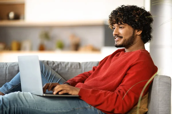 Fiatal Mosolygós Indiai Férfi Laptop Használata Közben Pihentető Kanapén Otthon — Stock Fotó