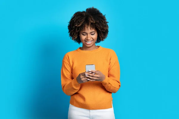 素晴らしいモバイルアプリ 青のスタジオの背景に隔離された男とチャット 広告のためのコピースペース ブランドの新しいスマートフォンや笑顔を使用してかなり中クールな若い黒人女性 — ストック写真