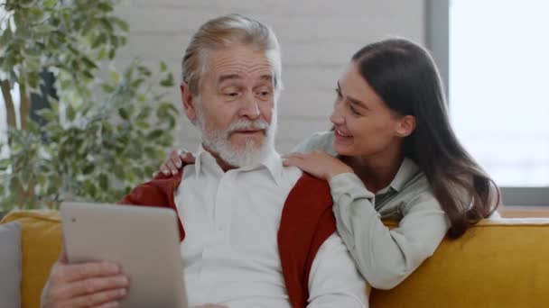 积极的老年人上网浏览数字平板电脑 阅读新闻 他漂亮的孙女过来拥抱他 一起讨论内容 跟踪镜头 慢动作 — 图库视频影像