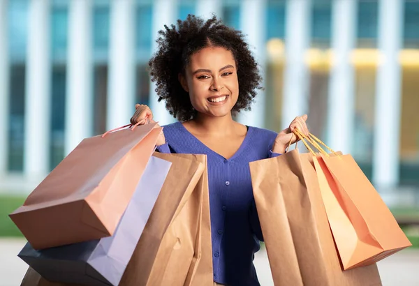 快乐的黑人妇女采购广告购物者提着纸袋站在商场附近 微笑着面对相机 大季节性销售广告概念 — 图库照片