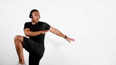 Beyaz stüdyo arka planında kablosuz kulaklık takan ve müzik dinleyen, diz kırma egzersizi yapan Afro-Amerikan sporcu. Fitness Egzersiz Çalma Listesi. Panorama, Boşluğu Kopyala