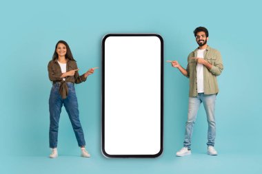 Sıradan güzel bir kadın ve beyaz ekranlı büyük cep telefonunu gösteren yakışıklı bir adam. Randevu uygulaması için model, mavi arka plan, tam boy.