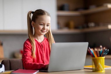 Çevrimiçi Eğitim. Evde dizüstü bilgisayarla gülümseyen küçük kız çalışması, liseli kız bilgisayar klavyesinde yazı yazması, ev ödevi yapması ya da internete göz atması, uzaktan öğrenmenin keyfini çıkarması, boşluğu kopyalaması.