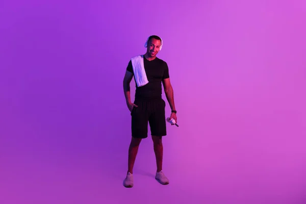 准备好做运动了全长拍摄的运动型黑人男子头戴耳机 听运动型演奏家的音乐 拿着一瓶水站在紫色霓虹灯的背景 健康健康 — 图库照片