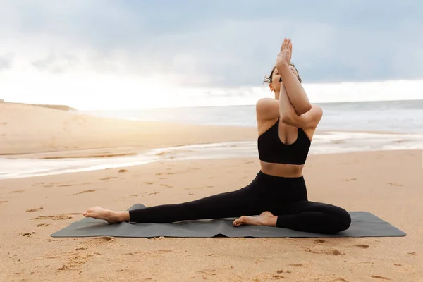 早上在室外做瑜伽 年轻女子参加户外运动服装训练 运动女子坐在瑜伽练习场的健身垫上 在近海海滩上锻炼 自由自在 — 图库照片