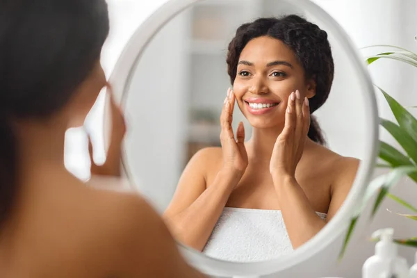 美の概念 浴室で鏡を見て魅力的な若い黒人女性 美しいアフリカ系アメリカ人女性は彼女の顔に触れ 反射に笑みを浮かべて スキンケアルーチンを楽しみます 選択的フォーカス — ストック写真