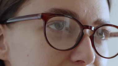 Görme sorunu. Gözlük takan ve cihaz üzerinde bilgi okuyan, rahatlıkla çalışan genç bir kadının portresini kapat.