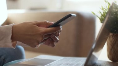 Modern hayattaki yetenekler. Tanımlanamayan bir kadının akıllı telefondan mesajlaşırken, sosyal medyada arkadaşlarıyla sohbet ederken, laptopun yanında otururken, yavaş çekimde, boş alanda.