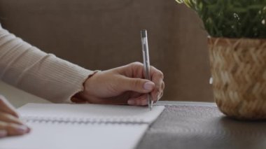 Fotokopi defterine yazı yazan, evde masa başında ders çalışan, boş alan olan tanınamaz solak kadının yakın plan fotoğrafını çek.