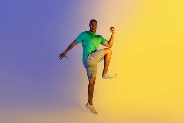 快乐运动的黑人小伙子练习手肘对膝盖站在蓝色和黄色的霓虹灯背景上 微笑对相机 全长快乐的有动力的运动员 Studio Shot — 图库照片
