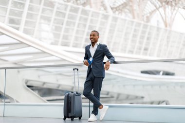 Havalimanı terminalinde pasaportu olan yakışıklı siyahi bir işadamı uçuş için bekleyen takım elbiseli bir Afrikalı Amerikalı, iş seyahatinin keyfini çıkarıyor, kopyalama alanı.