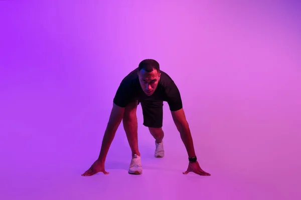 坚定的非洲裔美国运动员 准备在紫色霓虹灯背景下的蹲伏起跳位置 跑步者准备跑去看相机 体育动力 — 图库照片