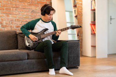 Kulaklık takan ve elektro gitarla akorlar çalan Japon ergen çocuk hafta sonları evde koltukta oturan müzik aleti çalmayı öğreniyor. Genç Müzisyen, Müzikal Tatil Konsepti