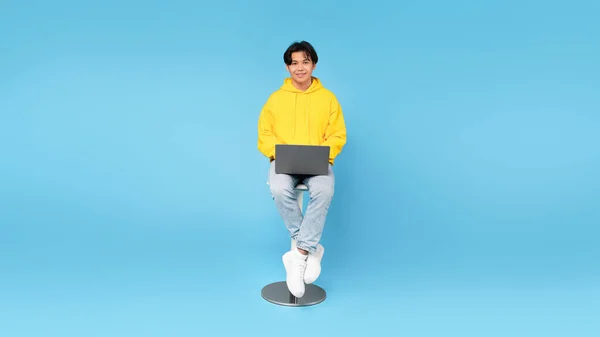 快乐的日本学生少年使用笔记本电脑上网和在线学习坐在椅子上的蓝色工作室背景 男孩使用教育网站 电子学习概念 — 图库照片