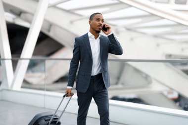 Havaalanında bavulla yürürken cep telefonuyla konuşan Afrikalı Amerikalı iş adamı, uçuş kapısına giderken cep telefonu konuşması yapan takım elbiseli genç siyah adam,