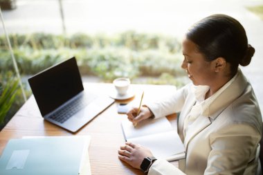 Beyaz takım elbiseli, gözlüklü, dizüstü bilgisayarlı, boş ekran ve bir fincan kapuçinolu genç bir bayanın kafenin içinde online ders vermesine sevindim. Modern iş ve çalışma, fikir yarat