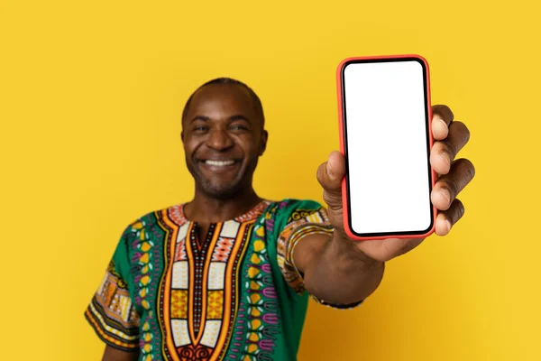 惊人的网上报价 快乐地微笑着 迷人的中年黑人 身穿鲜艳的非洲民族服装 拿着手机 在黄色的工作室里笑着 模仿着 — 图库照片