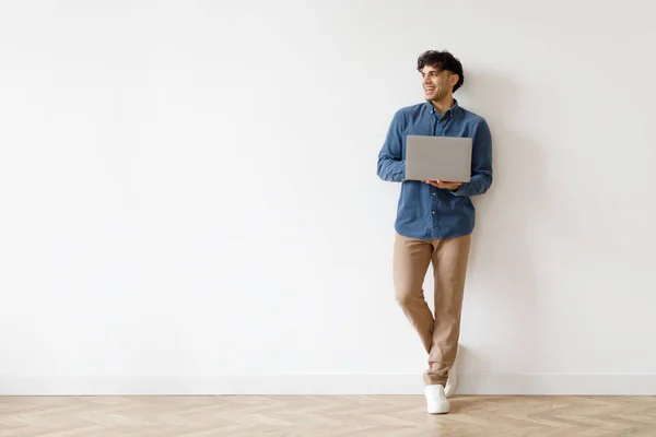 快乐的阿拉伯自由职业者男人拿着笔记本电脑在线广告卖出价 站在白墙近旁空旷的空间外张望 在家里上网的家伙 — 图库照片