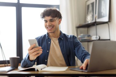 Neşeli Orta Doğulu Adam Modern Ofiste Dizüstü bilgisayarın başında oturan akıllı telefon mesajları kullanıyor. Sosyal Medya Uygulaması Uygulaması Uygulamasında İletişim ve Ağ kurmada Başarılı Genç İşadamı