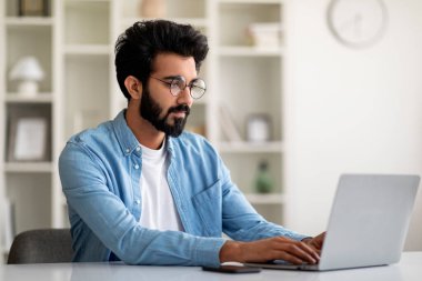 Bağımsız çalışma. İçişleri Bakanlığı 'nda bilgisayarla çalışan yakışıklı Hintli genç adam, dizüstü bilgisayarla masada oturuyor, milenyum doğusundaki adam cihaz ekranına bakıyor ve klavyede boş alan yazıyor.