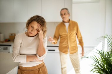 Kocasıyla tartışırken mutfakta ağlayan yaşlı bir kadın, evlilik krizi geçiren eşler, arka planda durup karısını suçlayan kızgın bir adam, seçici odaklanma.