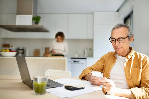 Uomo Anziano Che Usa Smartphone Seduto Tavola Con Laptop Cucina — Foto Stock