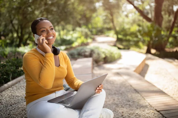 ラップトップや携帯電話で公園でリラックスした幸せな黒人女性 コンピュータを使用して 屋外で携帯電話で話す学生 外で休憩 コピースペース — ストック写真