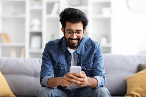 Fešák Mladý Indický Chlap Pomocí Smartphone Zatímco Odpočívá Gauči Doma — Stock fotografie