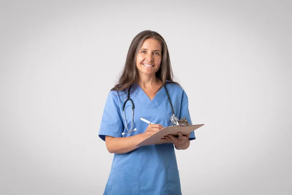Retrato Mujer Doctora Mayor Sonriente Uniforme Sujetando Portapapeles Sonriendo Cámara —  Fotos de Stock