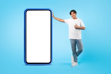 Bu uygulamayı sevdim. Koreli Öğrenci Poz Veriyor Büyük Akıllı Telefon Boş Ekran Onaylı Mobil Teklif Mavi Stüdyo Arkaplanı Üzerinde Hareketli. Mockup, Tam Uzunluk Çekimi