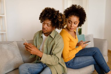 Sadakatsizlik. Sahipli siyah eş, evde koltukta oturan ve telefonuna gizlice bakan kocaları gözetliyor ve okuyor. Kadın İlişkisi Şüpheleniyor. İlişkide Kıskançlık Sorunu