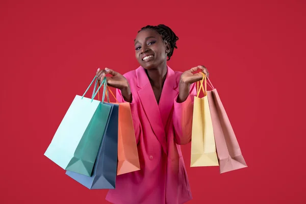 季節販売 幸せなスタイリッシュな黒女性保持明るいショッピングバッグと笑顔でカメラ 若いアフリカ系アメリカ人のお店の女性楽しむファッション 上の赤い背景 コピースペース — ストック写真