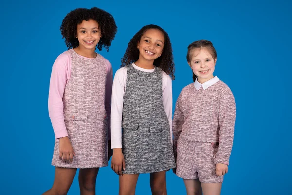 stock image Positive multiracial little girls in casual have fun, ready to study, look at camera isolated on blue background, studio. Friendship and education, ad and offer, children emotions