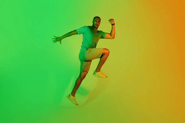 决心的黑人运动员男子跳跃和练习做肘部到膝盖有运动在绿色霓虹灯工作室背景 看相机 体育与健康概念 — 图库照片