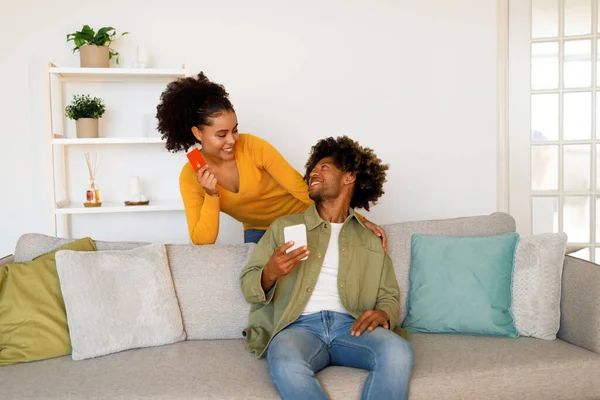 流动购物概念 快乐的非洲裔美国人夫妇使用手机和信用卡 在电子商务中一起购物应用坐在沙发上在家 银行付款申请 — 图库照片