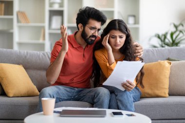 Mali Kriz Konsepti. Evdeki belgeleri kontrol eden Hintli çift, kanepede oturup gazete okuyan ve aile bütçesini yönetirken sıkıntı çeken doğu eşleri,